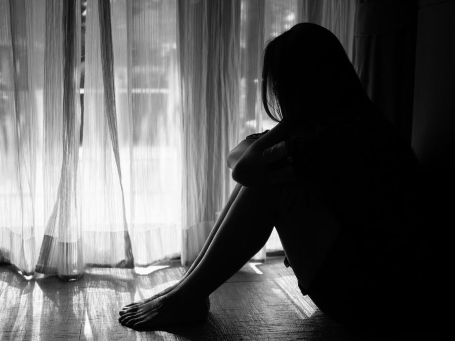 black and white of sad woman hug her knee and cry. Sad woman sitting alone in a empty room beside window or door